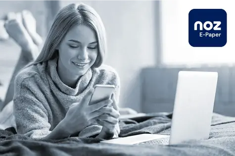 Eine Frau, die im Bett liegt und auf ihr Handy schaut. Neben ihr steht ein Laptop